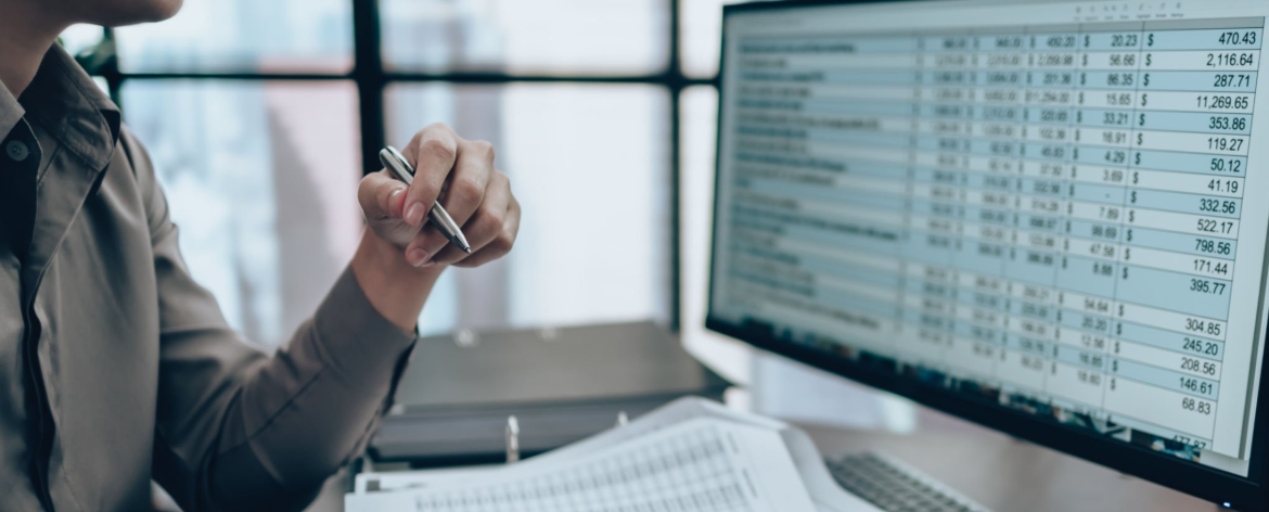 Professionnel analysant un tableau de données financières sur un écran d'ordinateur.